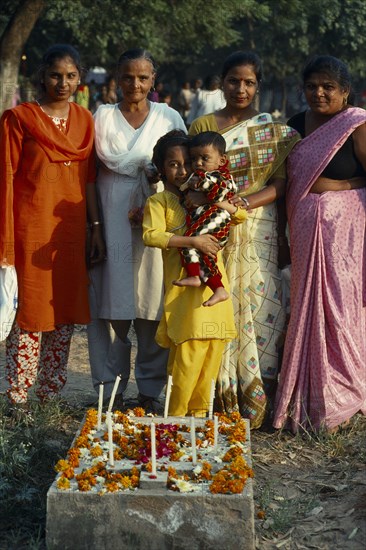 All Souls Day in Christian cemetary family group around grave decorated with flowers and candles.