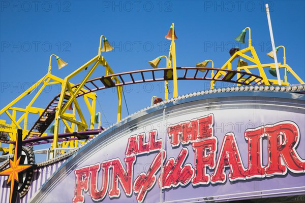 Sacade of amusement arcade with rollercoaster behind in clear blue sky.