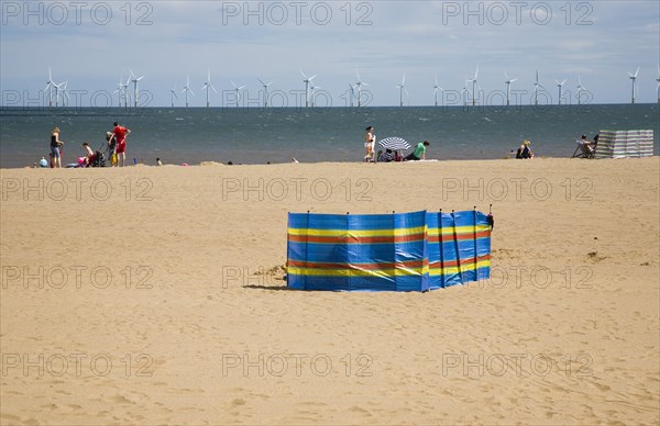 Wind Farm offshore on the horizon with families and windbreaks on the beach.