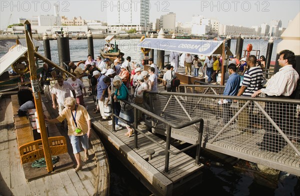 Tourists board Abra water taxi moored on the Creek with Bur Dubai heritage skyline behind.
