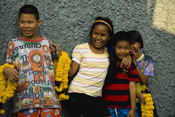 Thai children with mobile phone and floral garlands to celebrate the annual blessing of local temple .