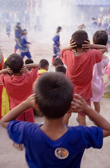 Thai boys cover their ears watching firecrackers exploding at local temple.