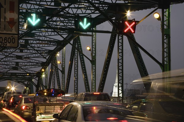 Traffic flow control in evening rush hour on Saphan Phut Memorial Bridge illuminated temple stupa in the background.