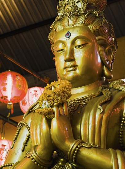 Gold Guanyin Goddess of Mercy statue with red lanterns for Chinese New Year.