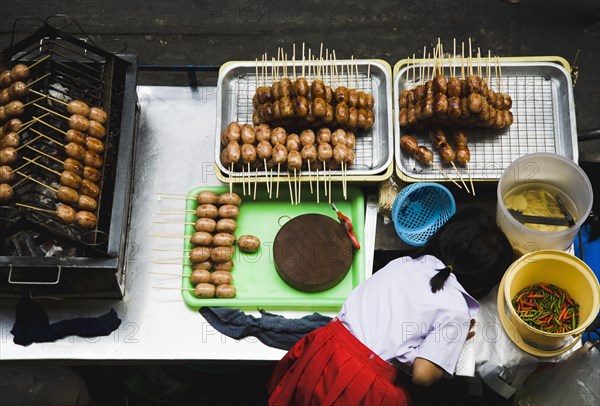 Primary School girl in uniform at sausage stall outside BTS Skytrain station.