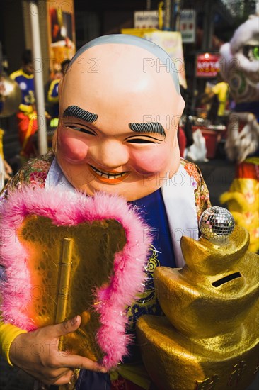 Member of dance troupe with papier mache character head and fan collecting money for Chinese New Year show.