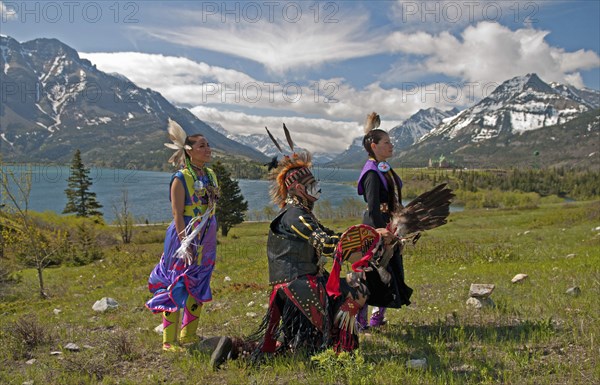 Blackfoot Indians dressed for a Pow Wow with Middle and Upper Waterton Lakes the Rocky Mountains and the Prince of Wales Hotel in the background. The park is a UNESCO World Heritage Site Blue sky with unusual cloud formation