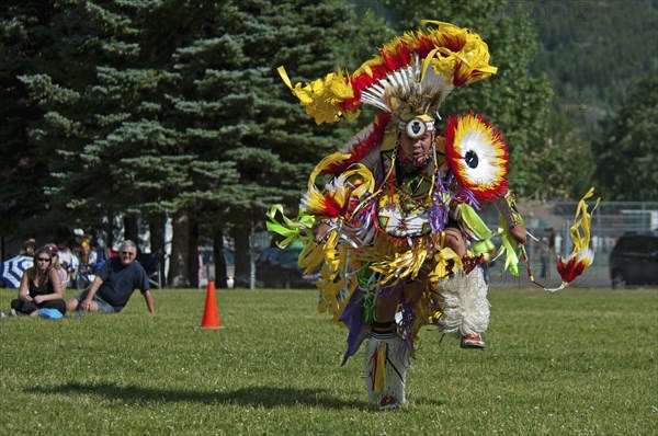 Blackfoot dancer in the Men's Fancy Dance at the Blackfoot Arts & Heritage Festival Pow Wow organized by Parks Canada and the Blackfoot Canadian Cultural Society Tourists sitting on grass watching spectacle