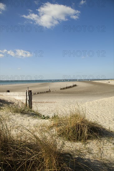 View across sand dunes towards beach and sea at East Head. Sunshine and blue sky.