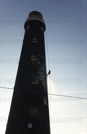 Man cleaning Lighthouse tower with pressure washer whilst abseiling.