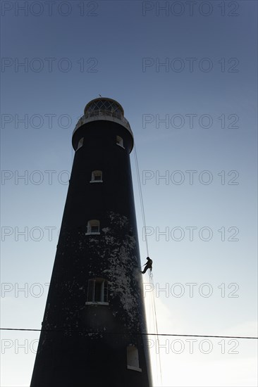 Man cleaning Lighthouse tower with pressure washer whilst abseiling.