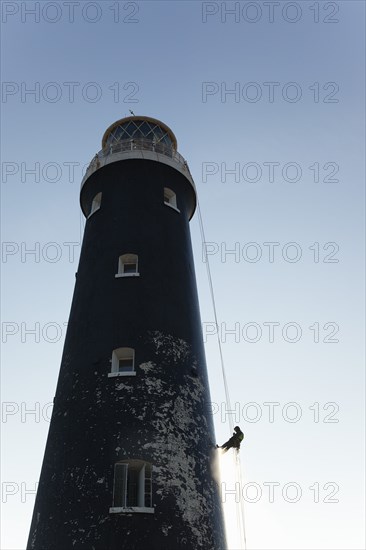 Man cleaning Lighthouse tower with pressure washer whilst abseiling.