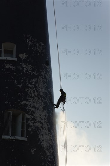 Man cleaning Lighthouse tower with pressure washer whilst abseiling.