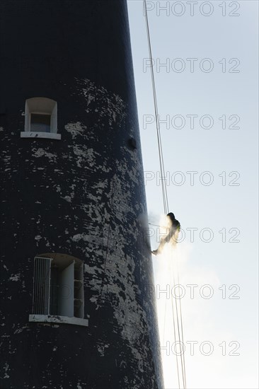 Man cleaning Lighthouse tower with pressure washer whilst abseiling.