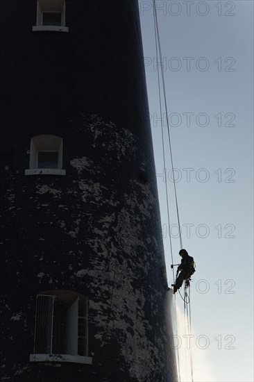 Man cleaning Lighthouse tower with pressure washer whilst abseiling.