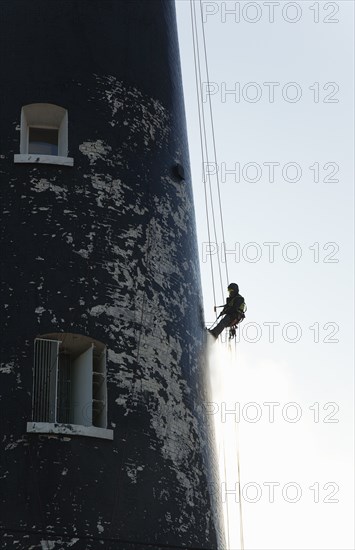 Man cleaning Lighthouse tower with pressure washer whilst abseiling.