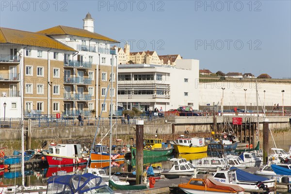 View over fishing boats moored in the Marina with apartment buildings behind.