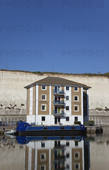 Apartment building in marina with moored barge and chalk cliffs behind.