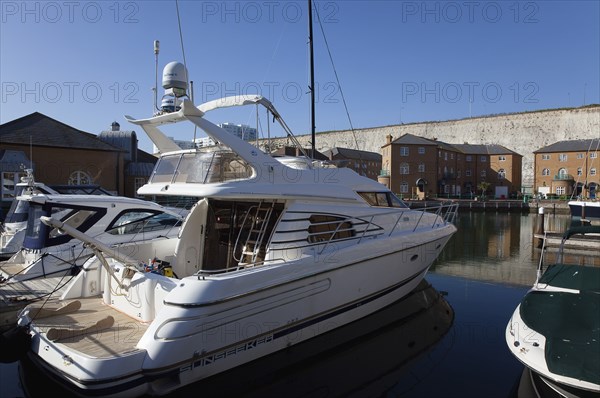 Apartment buildings in marina with moored motor boats and chalk cliffs behind.