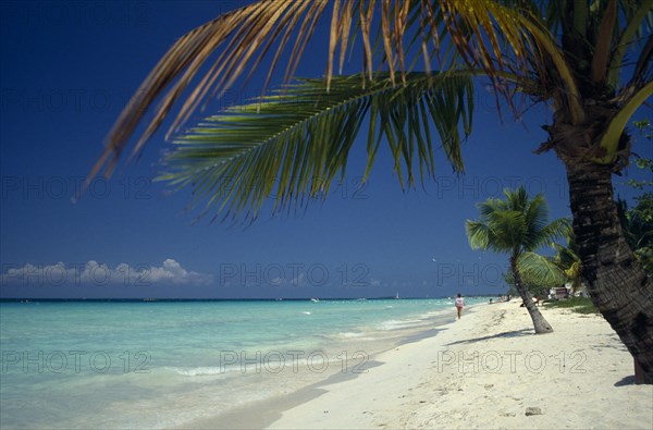 West Indies, Jamaica, Negril, Sandy stretch of beach beside flat aquamarine water with woman walking along shoreline in distance. Photo : David Cumming