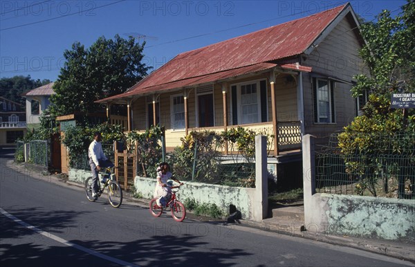 West Indies, Jamaica , Port Antonio, Roadside housing with veranda and walled garden. Boy and young girl cycling past. Photo : David Cumming