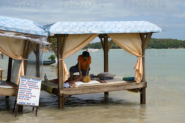 Thailand, Koh Samui , Chaweng Beach, Beach Massage on a four poster bench over the sea with a woman giving a man a massage with a sign displying prices for various treatments. Photo : Derek Cattani