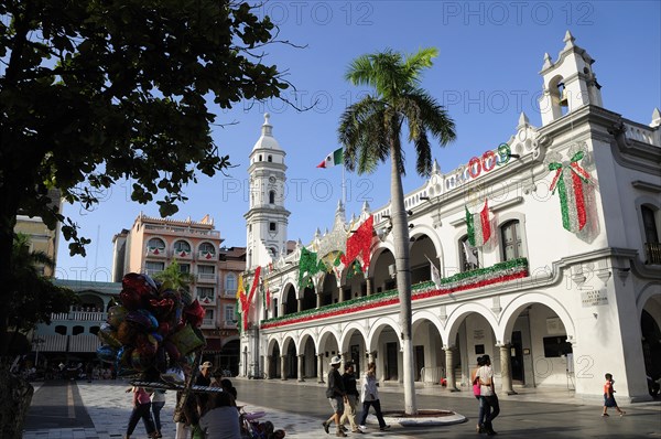 Mexico, Veracruz, The zocalo and government buildings decorated for Independence Day celebrations with balloon seller and tourists in the foreground part framed by tree. Photo : Nick Bonetti