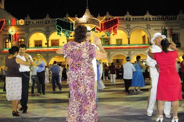 Mexico, Veracruz, Couples dancing in the Zocalo at night illuminated decorations in the national colours for Independence Day celebrations on building facade behind. Photo : Nick Bonetti