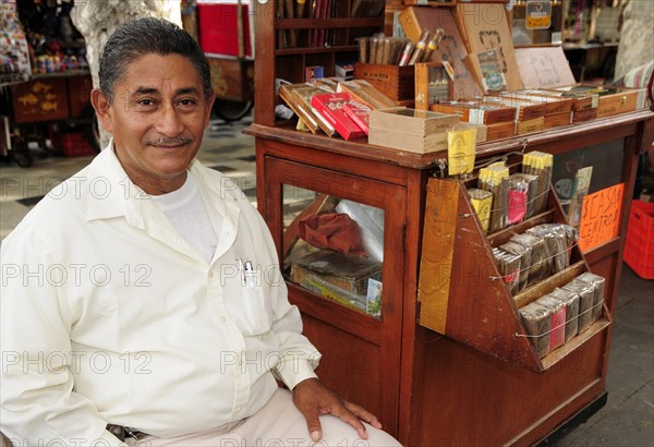 Mexico, Veracruz, Cigar seller in the Zocalo seated beside mobile stand with display of different cigars. Photo : Nick Bonetti