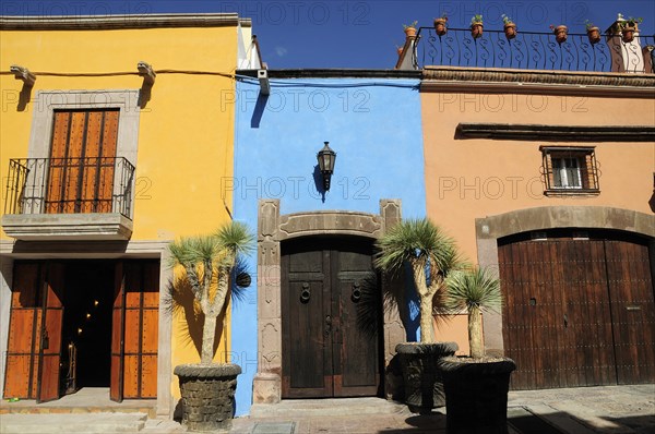 Mexico, Bajio, San Miguel de Allende, Colourful house facades on paved street with plant pots on roof balcony and outside wooden doors. Photo : Nick Bonetti