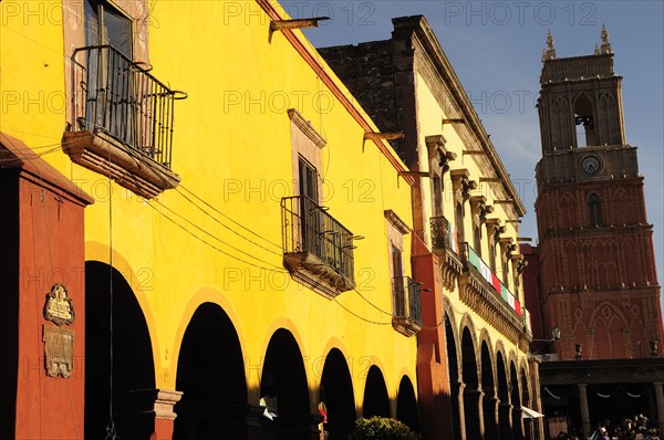 Mexico, Bajio, San Miguel de Allende, El Jardin Yellow facade of colonial mansion and arcades with clock tower beyond. Photo : Nick Bonetti
