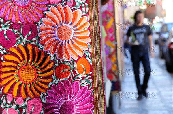 Mexico, Bajio, San Miguel de Allende, Brightly coloured embroidered textile hanging outside arts shop with flower design in pink red and orange. Photo : Nick Bonetti