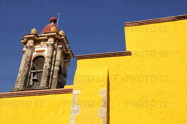 Mexico, Bajio, San Miguel de Allende, Part view of bright yellow exterior wall and church bell tower. Photo : Nick Bonetti