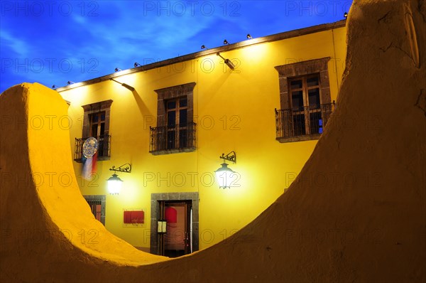 Mexico, Bajio, San Miguel de Allende, Half circle formed wall framing part view of opposite building at night with lighted lamps hanging from brackets at doorway. Photo : Nick Bonetti
