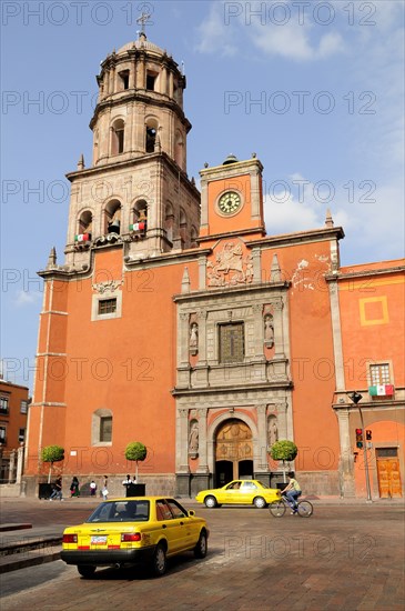 Mexico, Bajio, Queretaro, The church of San Francisco brightly coloured exterior facade with taxis and cyclist on road in foreground. Photo : Nick Bonetti