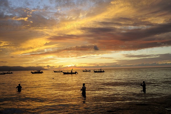 Mexico, Jalisco, Puerto Vallarta, Fishermen standing in sea with fishing boats at sunset. Photo : Nick Bonetti