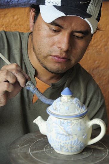 Mexico, Puebla, Talavera ceramic artist at Armando Gallery applying blue detail to raised design on teapot. Photo : Nick Bonetti