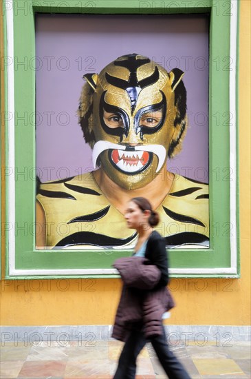 Mexico, Puebla, Young girl walking past poster of wrestler wearing mask and costume. Photo : Nick Bonetti