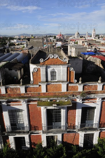 Mexico, Puebla, View across city rooftops with red brick and white facade of building in foreground. Photo : Nick Bonetti