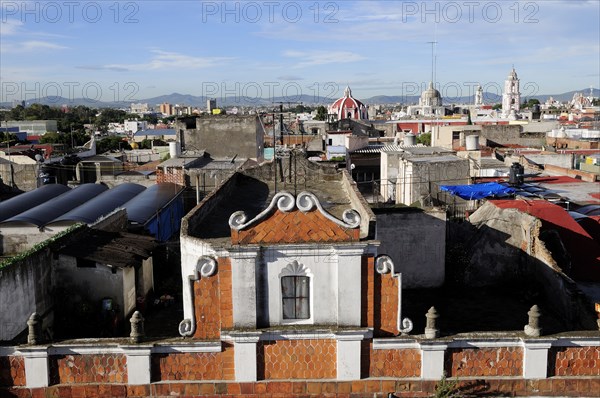 Mexico, Puebla, View across city rooftops with part view of red brick and white building facade in foreground. Photo : Nick Bonetti
