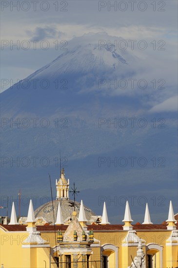 Mexico, Puebla, View of volcanic peak of Popocatepetl wreathed in cloud with Puebla rooftops in foreground. Photo : Nick Bonetti