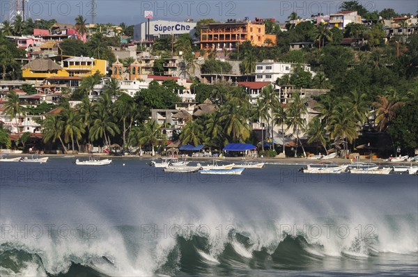 Mexico, Oaxaca, Puerto Escondido, Playa Principal Breaking waves and boats overlooked by buildings amongst palm trees.. Photo : Nick Bonetti