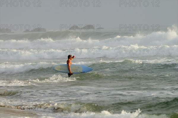 Mexico, Oaxaca, Puerto Escondido, Surfer walking through surf carrying board. Photo : Nick Bonetti