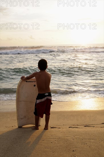 Mexico, Oaxaca, Puerto Escondido, Playa Zicatela Young body boarder standing on beach looking out to sea.. Photo : Nick Bonetti