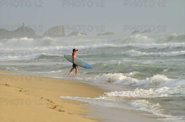 Mexico, Oaxaca, Puerto Escondido, Surfer walking into surf carrying board. Photo : Nick Bonetti