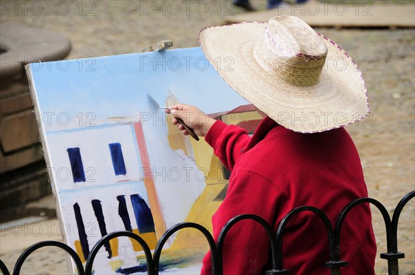 Mexico, Michoacan, Patzcuaro, Painter in Plaza Vasco de Quiroga applying paint to canvas using palette knife. Photo : Nick Bonetti