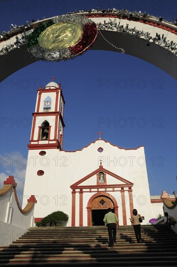 Mexico, Veracruz, Papantla, Cathedral de la Asuncion white and red painted exterior bell tower and steps to entrance framed by arch decorated for Independence Day celebrations.. Photo : Nick Bonetti