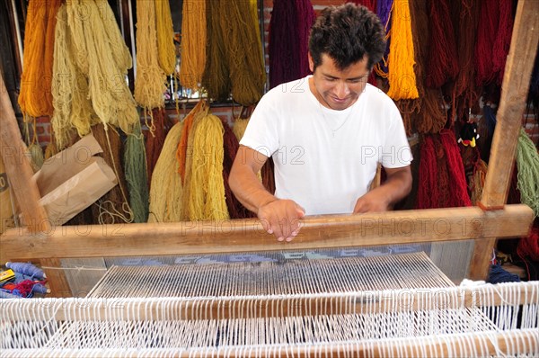 Mexico, Oaxaca, Teotitlan del Valle, Weaver at loom with different coloured yarn hanging in bundles behind.. Photo : Nick Bonetti
