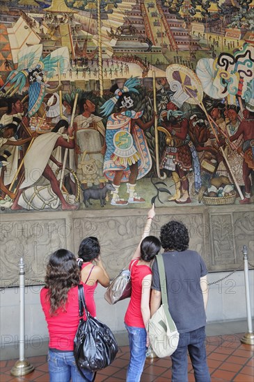 Mexico, Federal District, Mexico City, Group of visitors looking at mural by Diego Rivera depicting life before the Conquest in the Palacio Nacional. Photo : Nick Bonetti