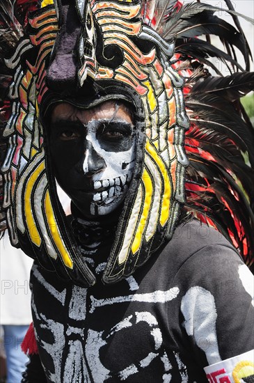 Mexico, Federal District, Mexico City, Portrait of Michacoa Aztec dancer in feather head-dress and painted face as Senor de Muerte or Mr Death performing in the Zocalo. Photo : Nick Bonetti